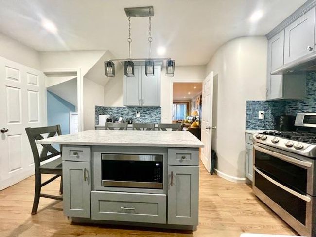 Kitchen featuring stainless steel appliances, light wood-type flooring, backsplash, and gray cabinetry | Image 4