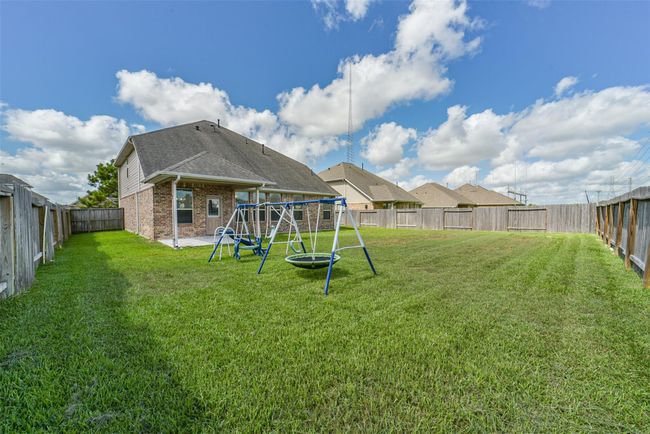 Spacious backyard with a swing set, lush green lawn, and a covered patio. Perfect for outdoor activities and relaxation, enclosed by a wooden fence for privacy. | Image 29