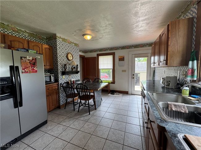 Kitchen featuring stainless steel refrigerator with ice dispenser, a sink, dark countertops, a textured ceiling, and decorative backsplash | Image 10