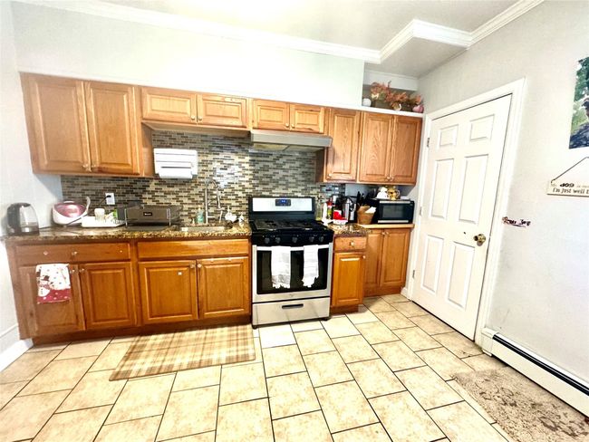 Kitchen featuring a sink, crown molding, stainless steel gas range, a baseboard radiator, and tasteful backsplash | Image 4