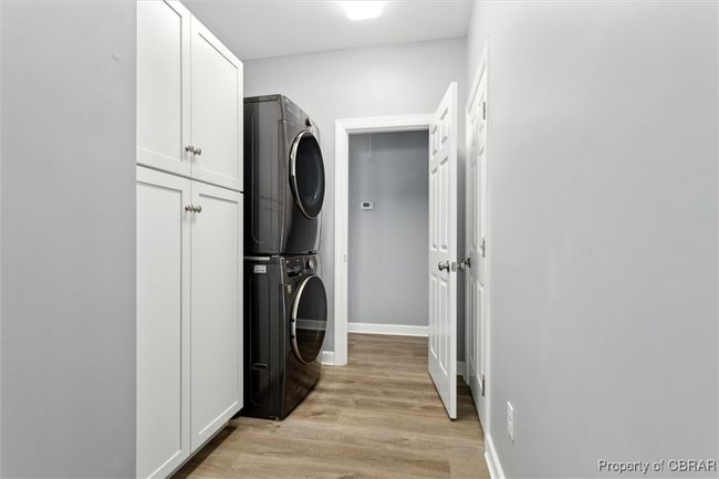 Clothes washing area with estacked washer and dryer, cabinet space, light wood-type flooring, and baseboards | Image 27