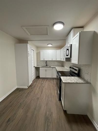 Kitchen featuring white cabinets, backsplash, stainless steel appliances, light stone countertops, and dark hardwood / wood-style flooring | Image 1