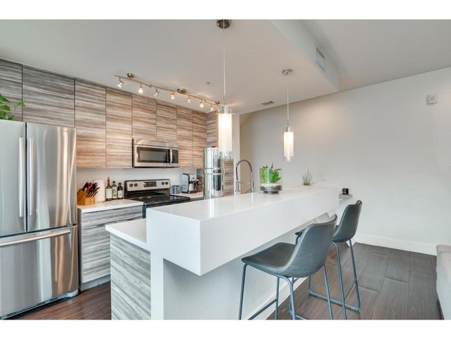 Kitchen with stainless steel appliances, a breakfast bar area, light countertops, dark wood finished floors, and hanging light fixtures | Image 10