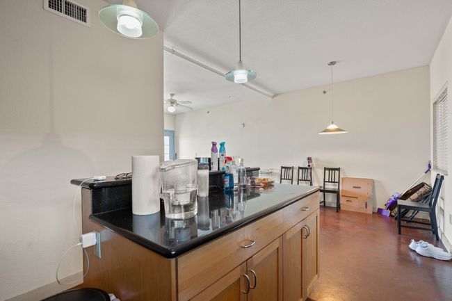 Kitchen featuring dark countertops, concrete flooring, hanging light fixtures, ceiling fan, and brown cabinets | Image 6