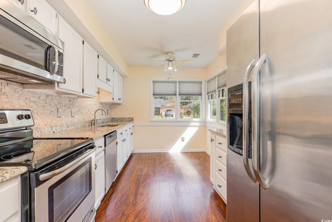 Kitchen with decorative backsplash, ceiling fan, stainless steel appliances, white cabinets, and dark wood-style flooring | Image 12