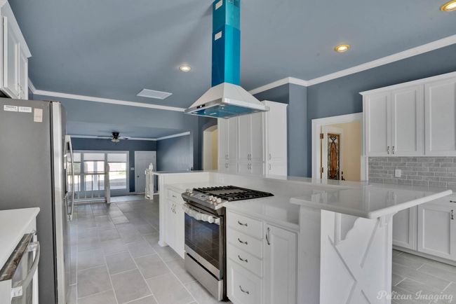 Kitchen featuring stainless steel appliances, a ceiling fan, island exhaust hood, tasteful backsplash, and white cabinets | Image 6