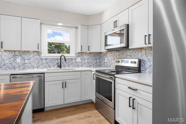 Kitchen with stainless steel appliances, wooden counters, decorative backsplash, and white cabinets | Image 9