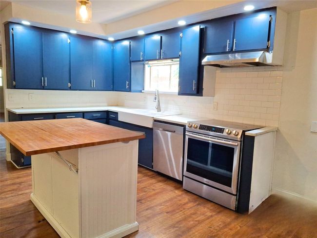 Kitchen with blue cabinetry, appliances with stainless steel finishes, under cabinet range hood, butcher block counters, and a sink | Image 5