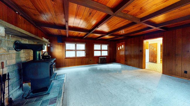 Unfurnished living room featuring a wood stove, wooden ceiling, radiator, coffered ceiling, and beamed ceiling | Image 6