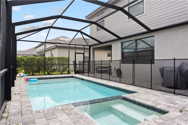 View of swimming pool featuring a pool with connected hot tub, glass enclosure, a grill, and a patio area | Image 36