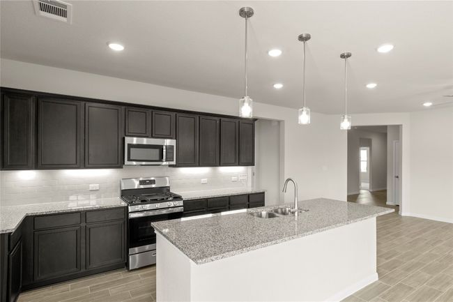 Kitchen featuring stainless steel appliances, wood finish floors, decorative backsplash, light stone countertops, and hanging light fixtures | Image 15