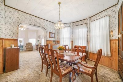 Carpeted dining room featuring ornamental molding, wood walls, and ceiling fan with notable chandelier | Image 3