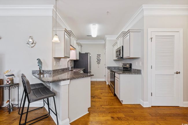 Kitchen with stainless steel appliances, a kitchen breakfast bar, a peninsula, wood finished floors, and dark stone countertops | Image 8