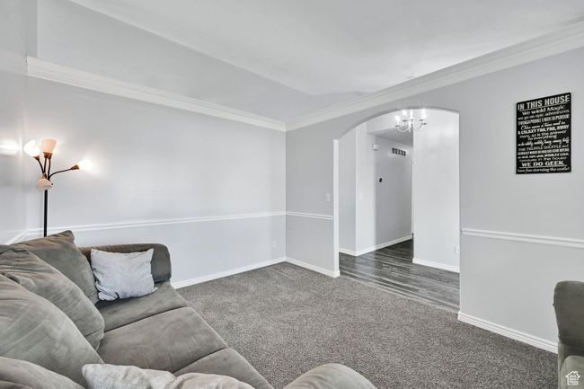 Living area with ornamental molding, baseboards, arched walkways, dark carpet, and a notable chandelier | Image 7
