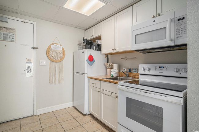 Kitchen featuring white appliances, white cabinetry, light tile patterned floors, a paneled ceiling, and light countertops | Image 10