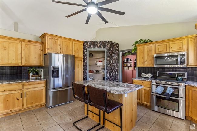 Kitchen with appliances with stainless steel finishes, backsplash, light tile patterned floors, ceiling fan, and light stone countertops | Image 6