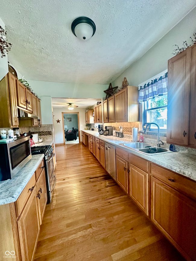 kitchen with stainless steel appliances, a textured ceiling, under cabinet range hood, light wood-style flooring, and tasteful backsplash | Image 16