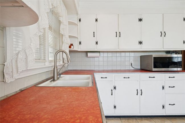 Kitchen with open shelves, a sink, decorative backsplash, white cabinets, and stainless steel microwave | Image 24