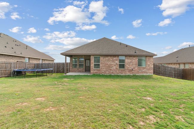 Back of house featuring a patio, a fenced backyard, a trampoline, brick siding, and a lawn | Image 23