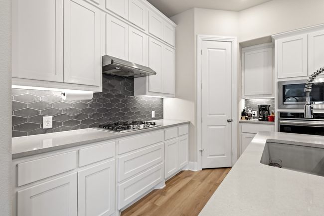 Kitchen with under cabinet range hood, stainless steel appliances, white cabinets, and light countertops | Image 10