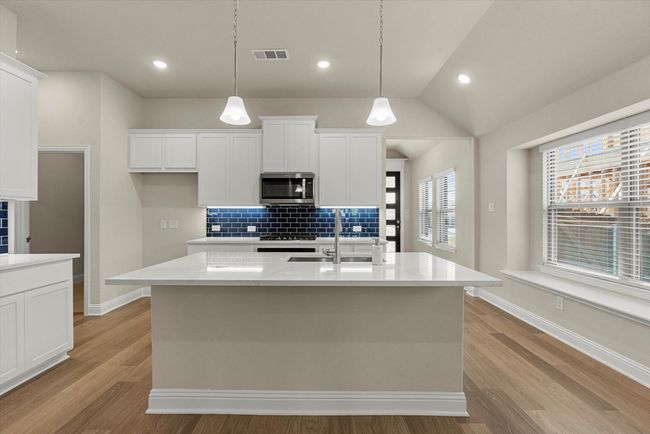 Kitchen featuring stainless steel microwave, decorative backsplash, light wood floors, white cabinetry, and recessed lighting. | Image 6