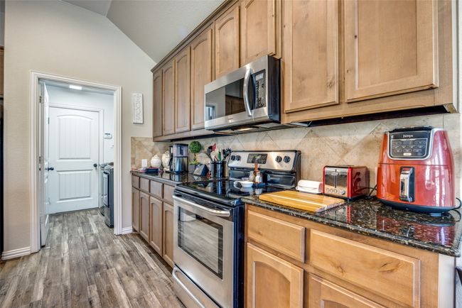 Kitchen with vaulted ceiling, decorative backsplash, dark stone counters, stainless steel appliances, and dark wood-type flooring | Image 7