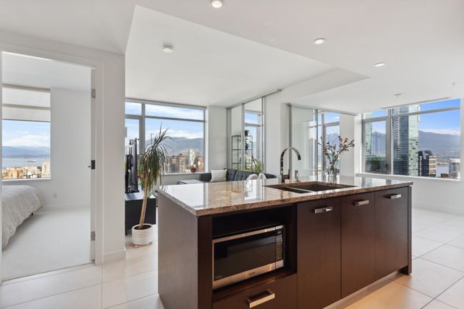 Kitchen featuring stainless steel microwave, dark brown cabinets, a sink, open floor plan, and a center island with sink | Image 6