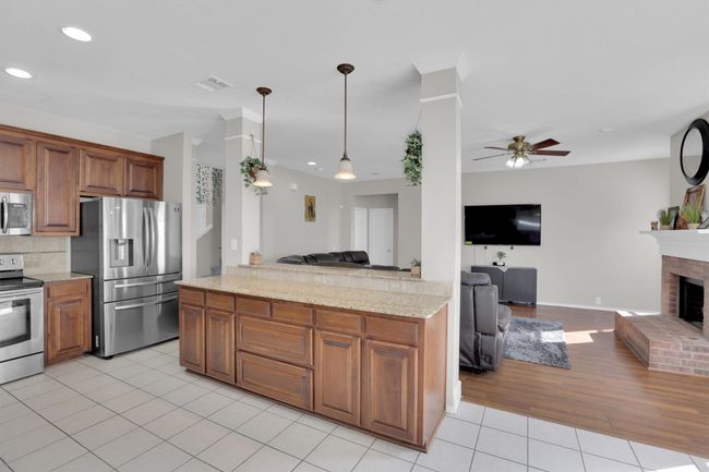 Kitchen featuring light tile patterned floors, stainless steel appliances, hanging light fixtures, a brick fireplace, and open floor plan | Image 14