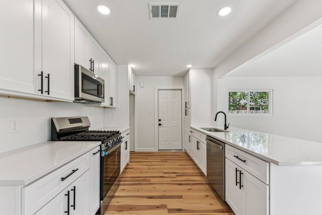 Kitchen with stainless steel appliances, light stone countertops, white cabinetry, light wood-style floors, and recessed lighting | Image 9