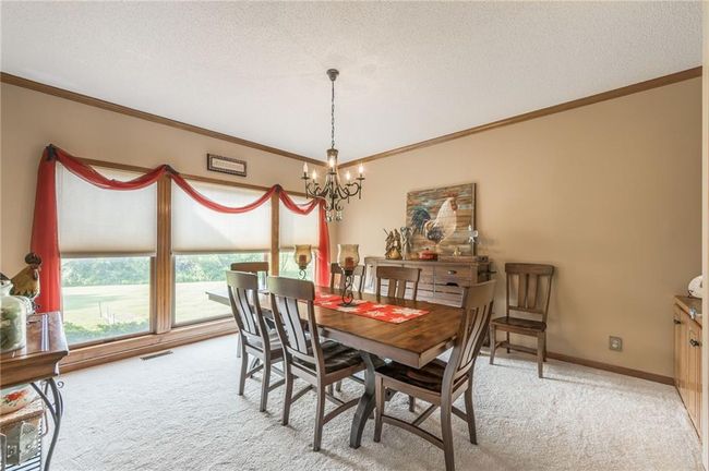 Dining room with a textured ceiling, ornamental molding, an inviting chandelier, visible vents, and light colored carpet | Image 21