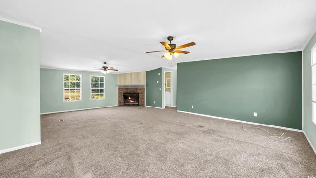 Unfurnished living room featuring ceiling fan, carpet floors, ornamental molding, and a brick fireplace | Image 4