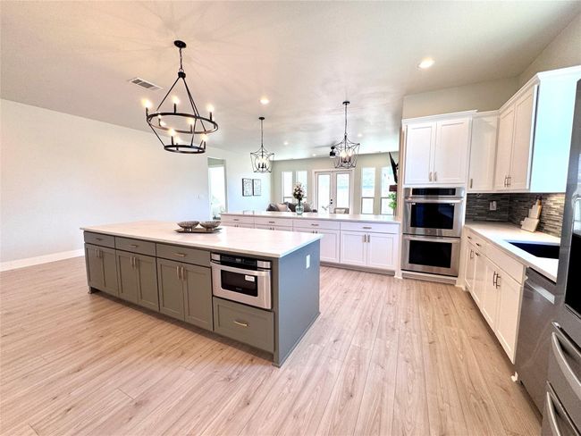 Kitchen with appliances with stainless steel finishes, a chandelier, light countertops, white cabinetry, and light wood-type flooring | Image 9
