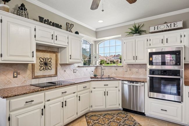 Kitchen featuring stainless steel appliances, dark stone countertops, a ceiling fan, white cabinetry, and crown molding | Image 14