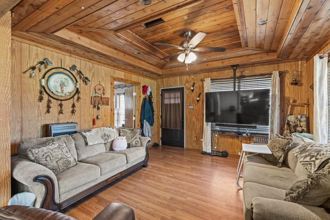 Living room featuring wood walls, wooden ceiling, a ceiling fan, wood finished floors, and lofted ceiling | Image 6