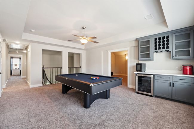 Recreation room featuring wine cooler, a tray ceiling, attic access, light carpet, and a ceiling fan | Image 29