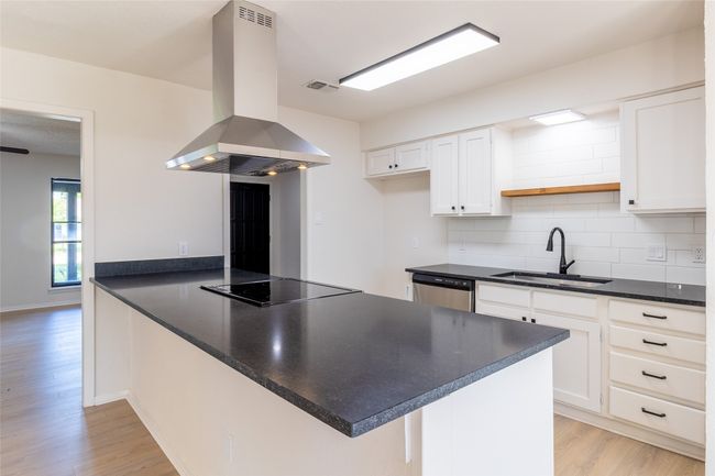 Kitchen featuring island range hood, stainless steel dishwasher, a sink, black electric stovetop, and a peninsula | Image 8