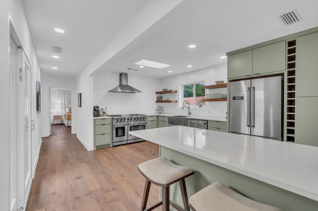Kitchen featuring wall chimney range hood, premium appliances, green cabinetry, and open shelves | Image 16