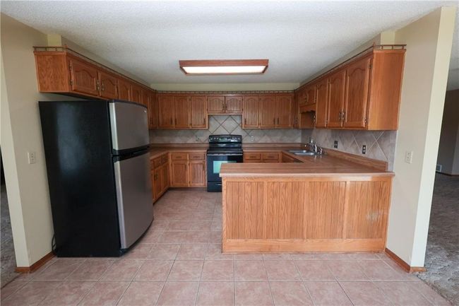 Kitchen with freestanding refrigerator, black range with electric stovetop, a peninsula, light countertops, and decorative backsplash | Image 16