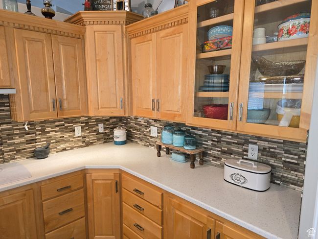 Kitchen with tasteful backsplash, glass insert cabinets, light stone counters, and light brown cabinetry | Image 15