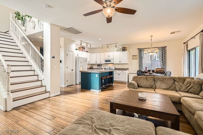 Living room featuring light wood-type flooring, ceiling fan with notable chandelier, stairs, and visible vents | Image 4