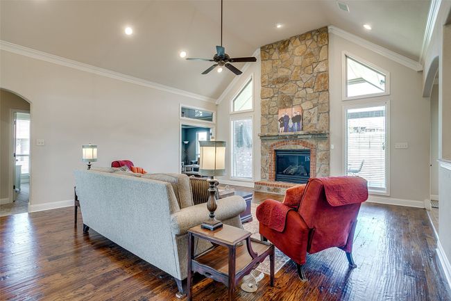 Living area featuring arched walkways, a stone fireplace, a ceiling fan, dark wood-style floors, and crown molding | Image 8