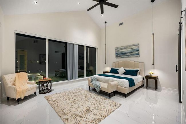 Indulge in the epitome of luxury in this exquisite primary suite, where dramatic vaulted ceilings and sophisticated pendant lighting set the tone for elegance. Floor-to-ceiling windows frame serene views of your private outdoor oasis, while gleaming marble-inspired floors and a soft, neutral color palette evoke a sense of calm sophistication. This is more than a bedroom—it’s your personal sanctuary. | Image 21