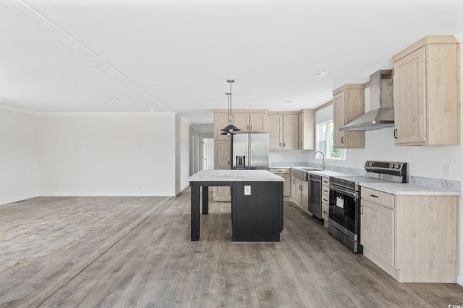 Kitchen with stainless steel appliances, wall chimney range hood, light brown cabinetry, a center island, and ornamental molding | Image 14