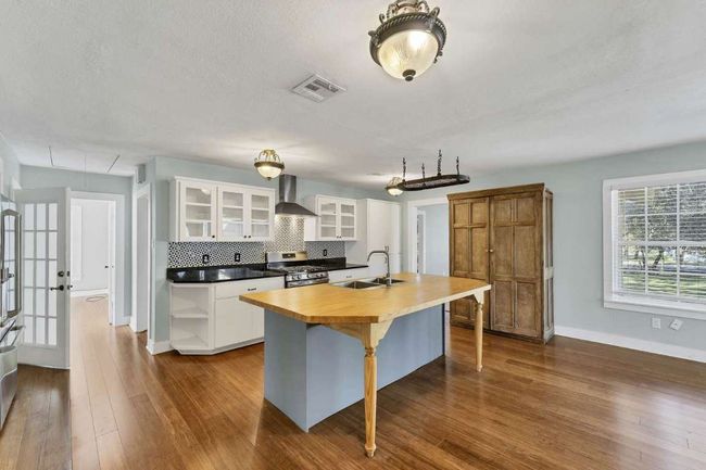 Kitchen featuring an island with sink, wall chimney range hood, visible vents, gas stove, and a sink | Image 6