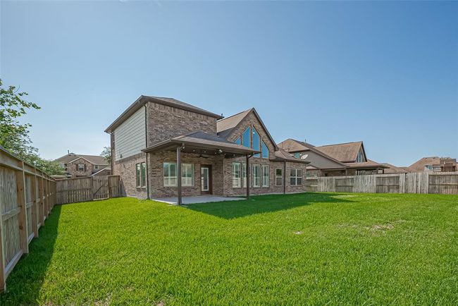 Modern two-story brick house with a spacious, well-maintained backyard. The home features large windows and a covered patio, all enclosed by a wooden fence, offering privacy and ample space for outdoor activities. | Image 43
