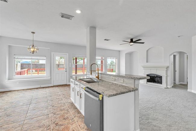 This photo showcases a bright, open-concept living space with a modern kitchen featuring granite countertops and a sink on the island. There’s a cozy fireplace in the carpeted living area and large windows offer natural light and views of the outdoor deck. | Image 17