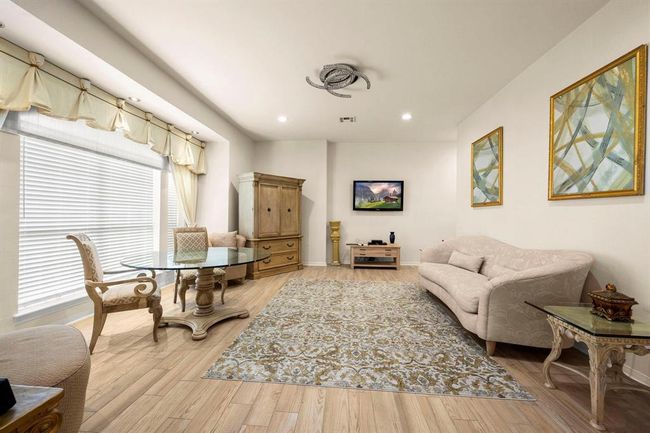 Spacious, well-lit room with elegant furnishings, hardwood floors, and modern amenities including a mounted flat-screen TV. Features decorative window treatments and a neutral color palette. | Image 26