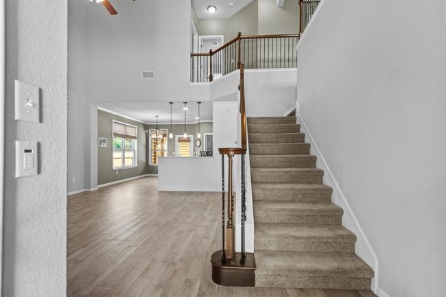 Staircase featuring wood finished floors, a towering ceiling, baseboards, and a ceiling fan | Image 9