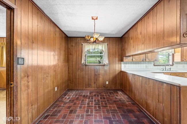 Unfurnished dining area featuring a sink, brick floors, a chandelier, healthy amount of natural light, and wooden walls | Image 16