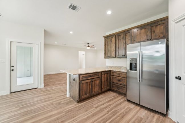 Kitchen featuring a peninsula, Vinyl Wood Plank floor, visible vents, light stone countertops, and stainless steel refrigerator with ice dispenser | Image 19